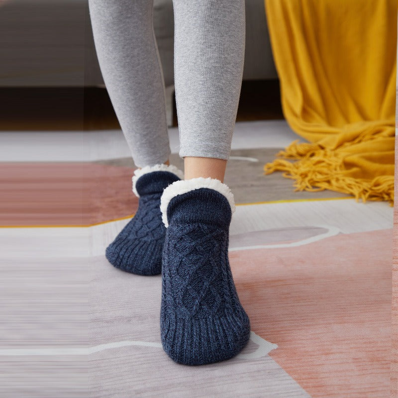 Person wearing dark blue cable knit socks with white cuffs on a wooden floor.